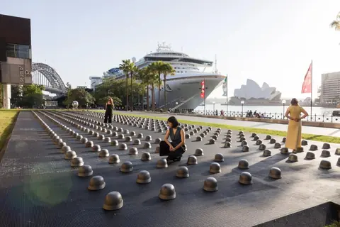 Ai Weiwei instaliacija „Mushrooms“ (2026): 500 ketaus kovinių šalmų eilėmis Tallawoladah vejoje prie MCA Australia Sidnėjuje